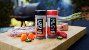 Two Skip's Peppers jars on a cutting board with seasoned meat and peppers
