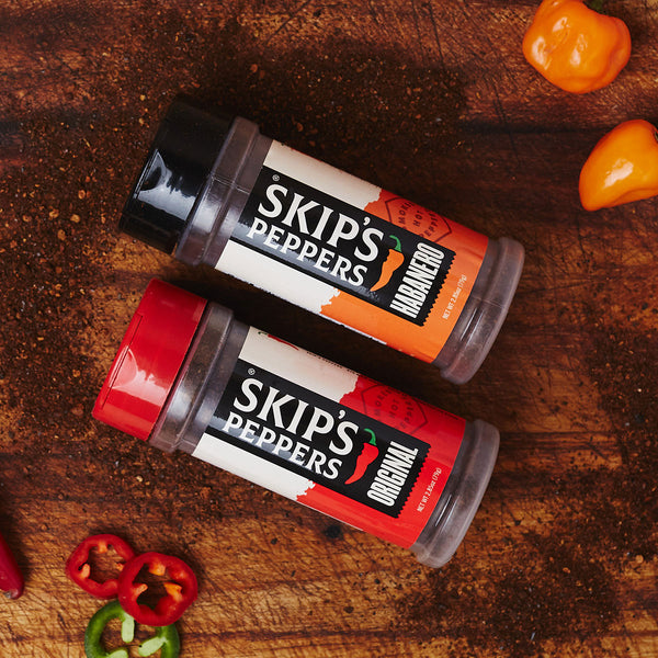 Two Skip's Peppers blend jars on a cutting board with red, green, and orange peppers